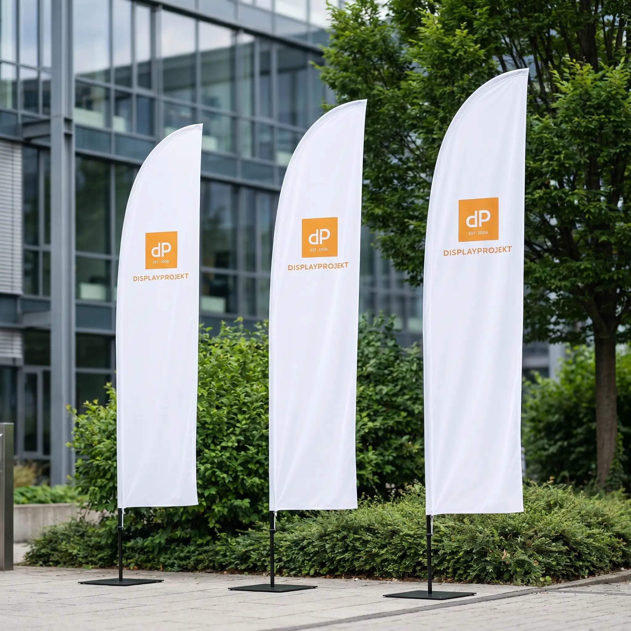 Tre vita fjäderformade flaggor med Displayprojekt-logotyp framför modern byggnad
